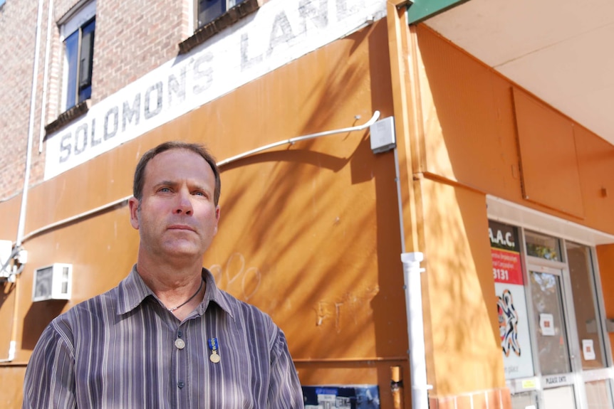 A man stands below an old sign which says 'Solomon's lane' in a town street.