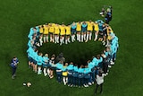 A group of Matildas players and coaches form a heart on the pitch as they talk after a big match.