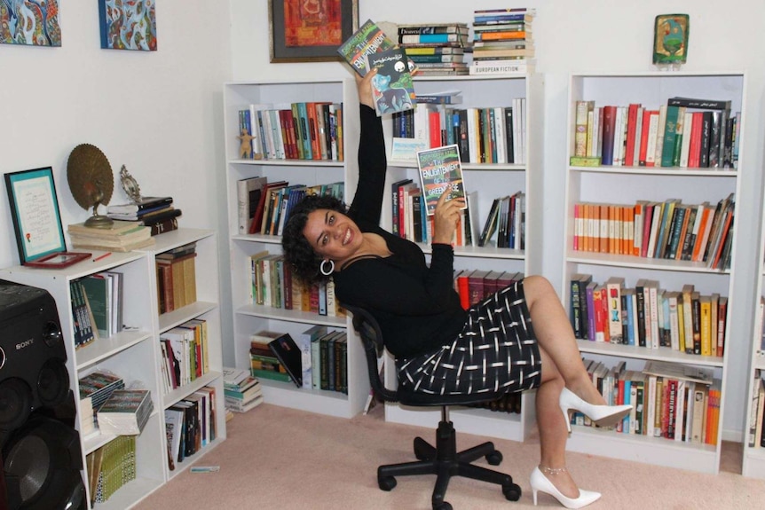 Iranian-Australian writer Shokoofeh Azar sitting in front of her bookshelf holding her books