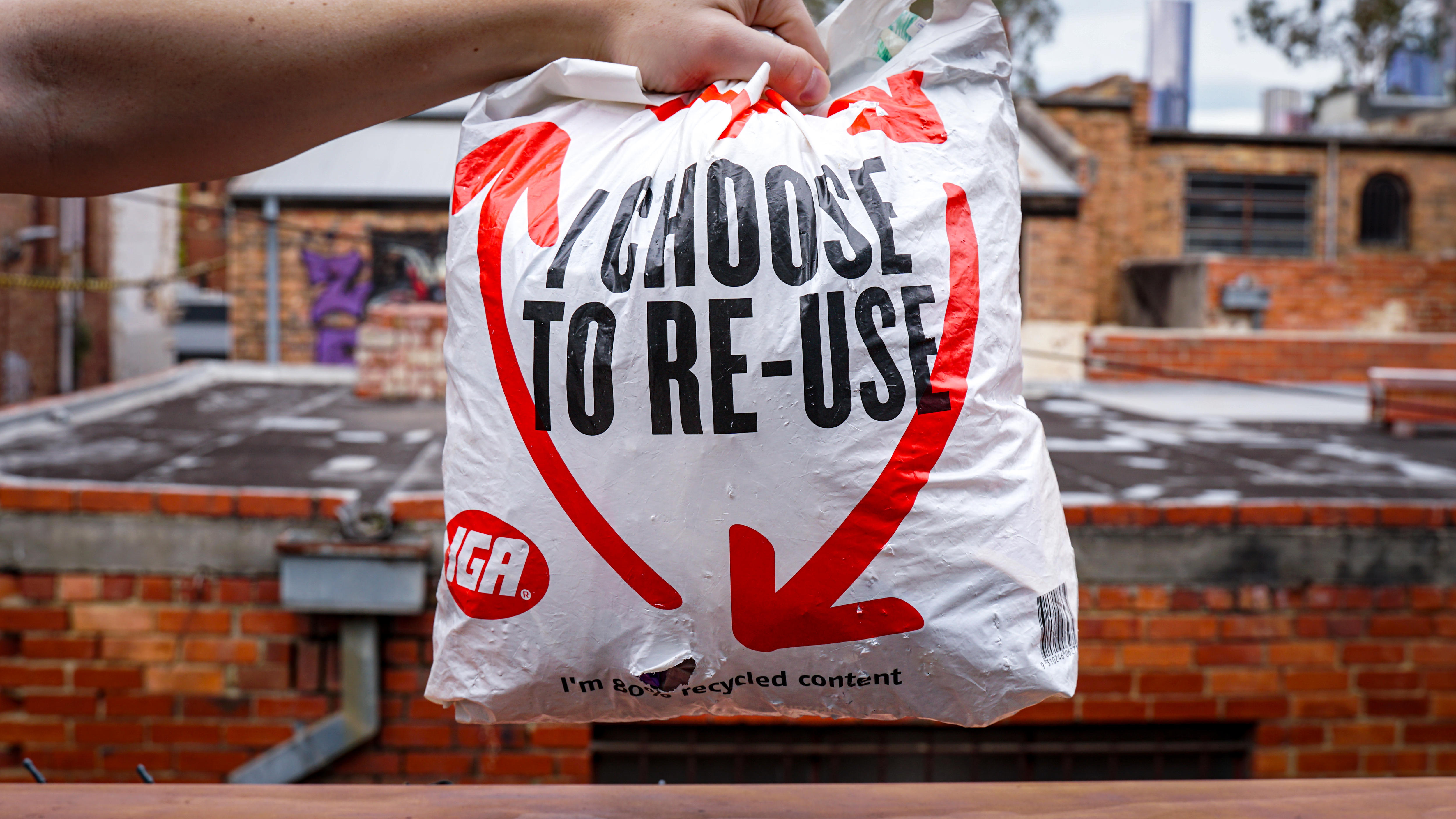 A person holds a plastic bag with the slogan 'I choose to re-use' on the front.