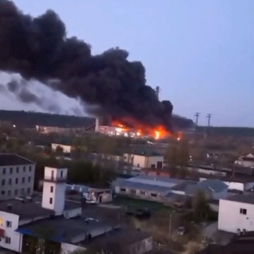 Smoke and fire coming from a building in the distance with more buildings in the foreground.