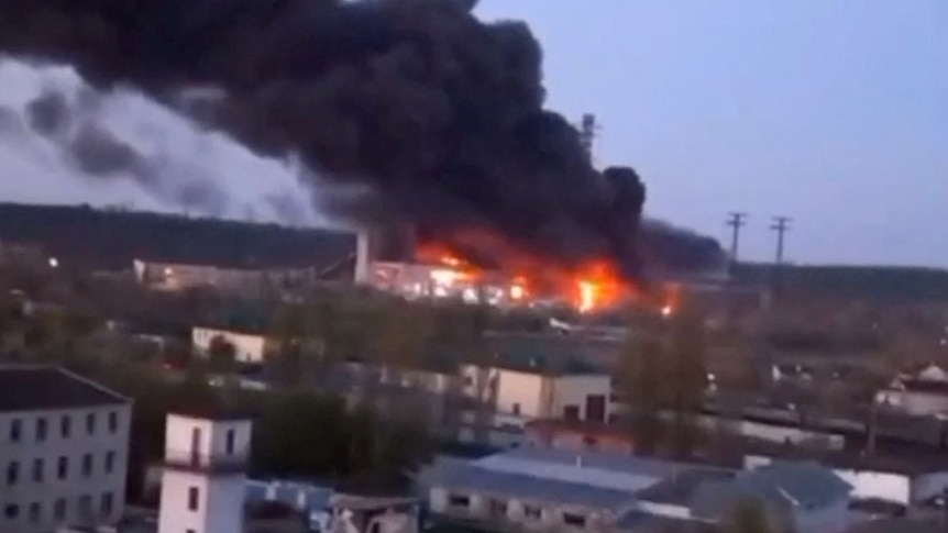 Smoke and fire coming from a building in the distance with more buildings in the foreground.