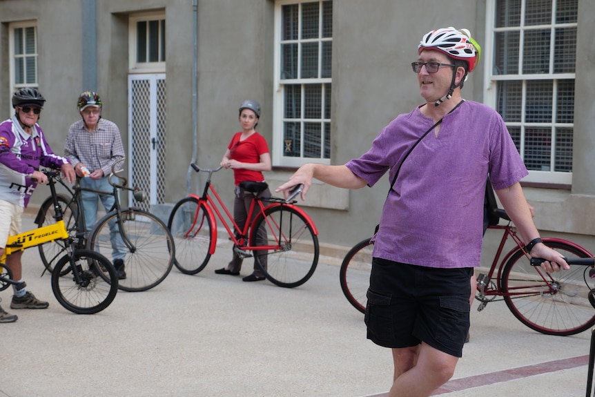 A man in a purple shirt and bike helmet with a bike, standing in a group of others with bikes