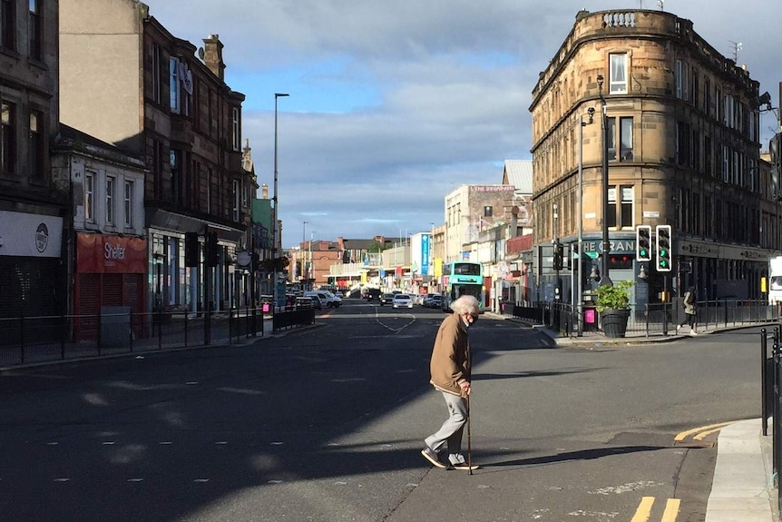 A view of a street in Glasgow, with a man walking across the road in a mask