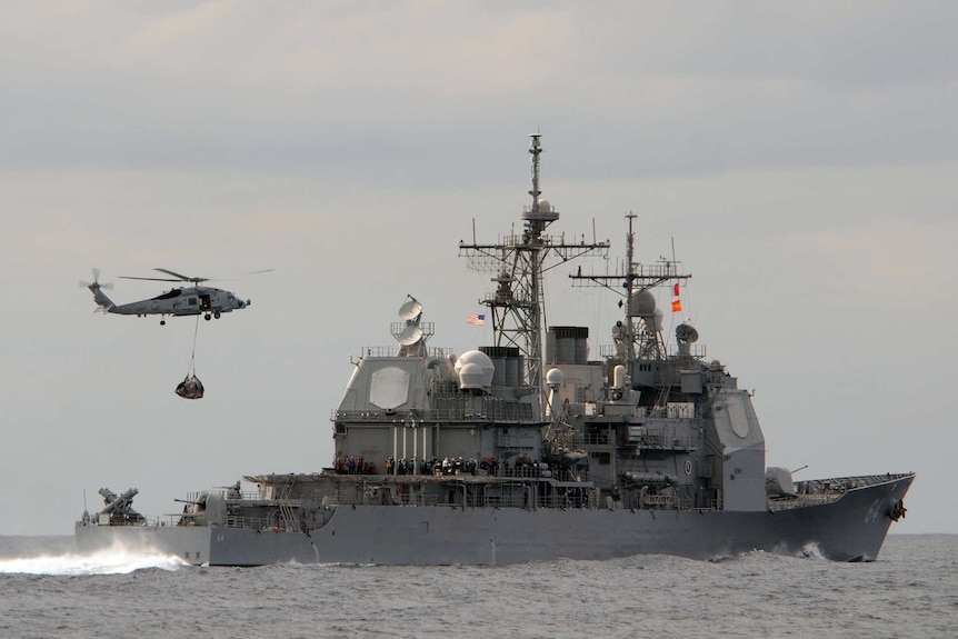 A helicopter hovers over the USS Gettysburg.