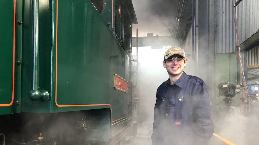 Trainee fireman Brock Sutton stands beside a steam train.