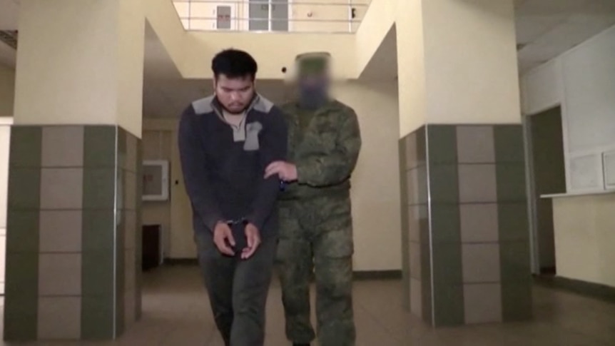 A Russian guard holds a prisoner while walking