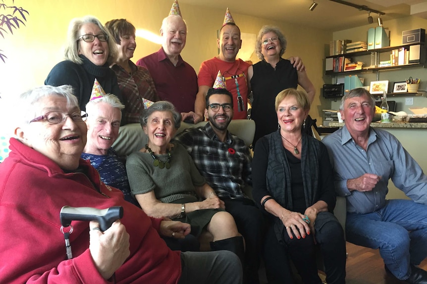 A group of people, some sitting on a couch, smile as they look at a camera.