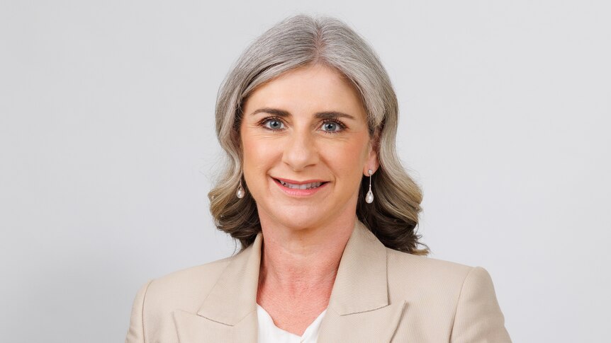 A woman with medium-length, neat grey hair poses in front of blank background.
