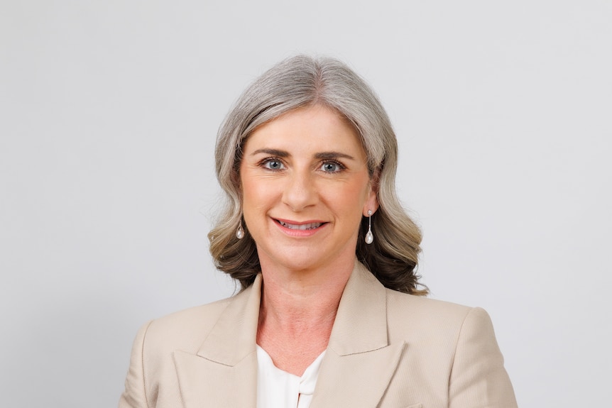 A woman with medium-length, neat gray hair poses in front of a blank background.