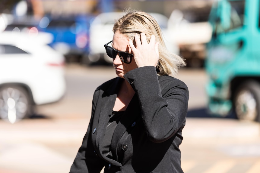A woman brushes her hair with her hand as she walks into a court trial.   