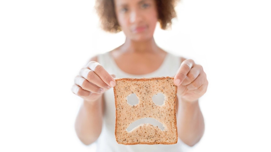 A woman holds a slice of bread cut into a sad face.