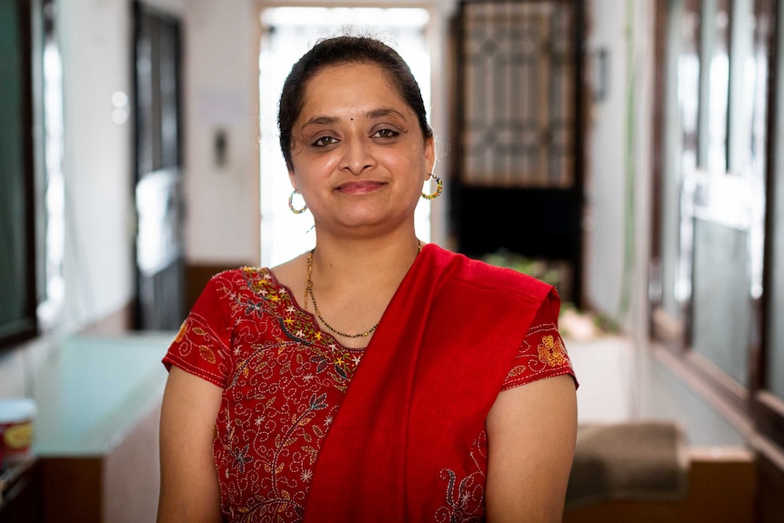 An Indian woman in a red sari with a slight smile on her face