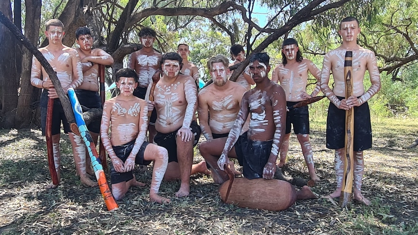 A group of young men gathered with Indigenous painting on their body and holding didgeridoos