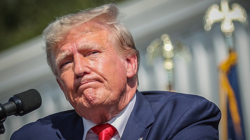 Trump grimaces as he speaks at a rally outside in the hot sun, with sweat visible on his face.