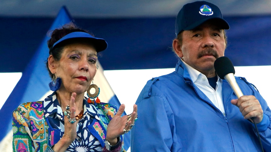 Nicaragua's President Daniel Ortega holds a microphone. Beside him his wife, Vice-President Rosario Murillo, claps