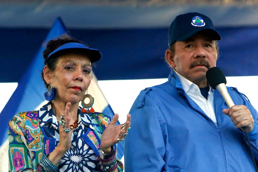 Nicaragua's President Daniel Ortega holds a microphone. Beside him his wife, Vice-President Rosario Murillo, claps