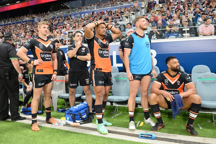 A group of Rugby players in orange and black kits look on with anguish from sideline of packed stadium