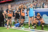 A group of Rugby players in orange and black kits look on with anguish from sideline of packed stadium