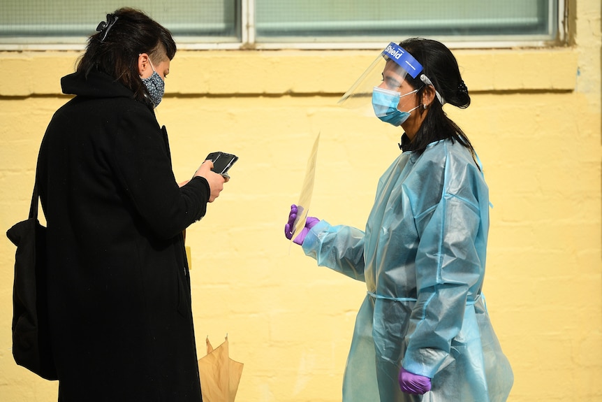 A healthcare worker is seen speaking to a person waiting in a line to receive a COVID-19 test