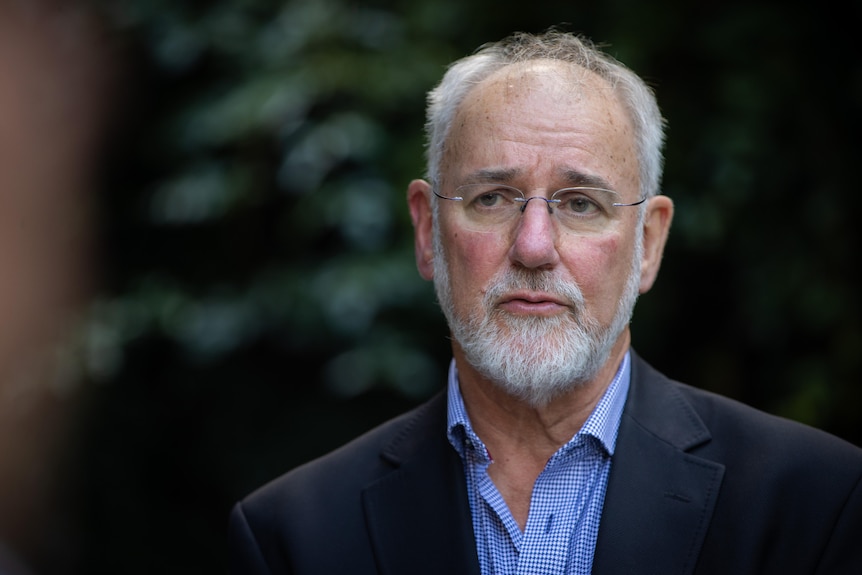 A balding man with silver hair and beard looks off camera