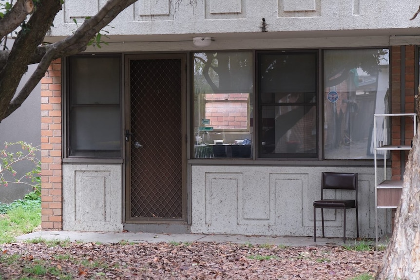 A front of a unit, with a concrete and glass front and a chair sitting in front of it