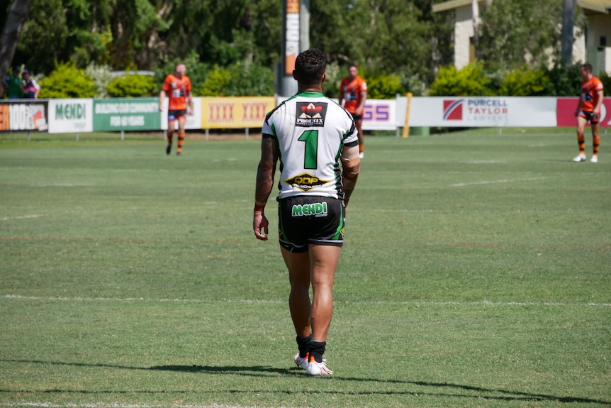 Young man wearing a green and white football jersey standing on football field 