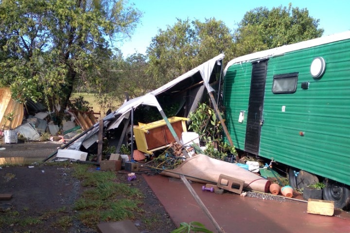 A pile of discarded furniture lies under a collapsed awning, leaning against a bright green caravan.
