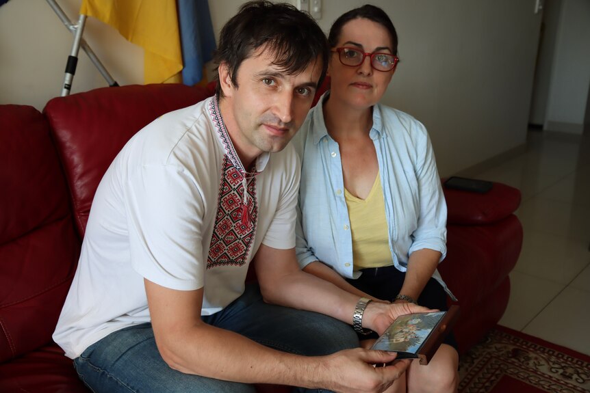 Portrait of a husband and wife sitting on a couch holding a family photo.