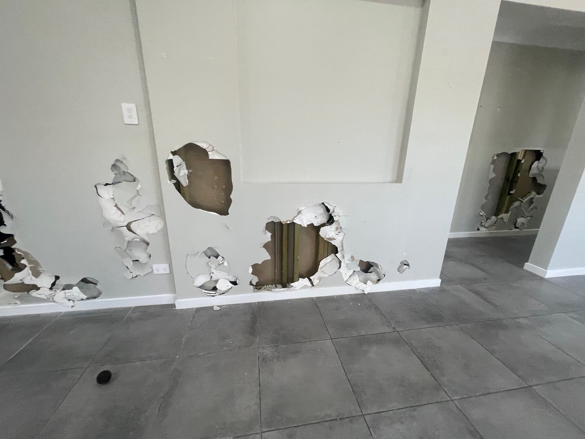 Damaged white walls with large holes exposing pipes and insulation.