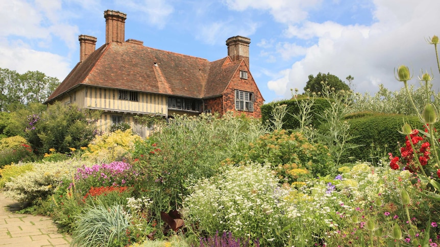 A historic timber-framed manor house is surrounded by a colourful planted garden.