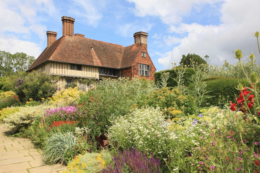 A historic timber-framed manor house is surrounded by a colourful planted garden.