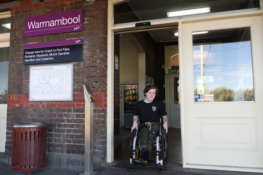 A man in a wheelchair rolls through an automatic doorway onto a train station