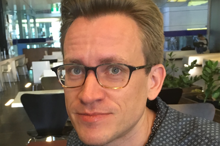 Jesse Olsen wearing glasses and a dark blue shirt with silver details in an empty coffee shop