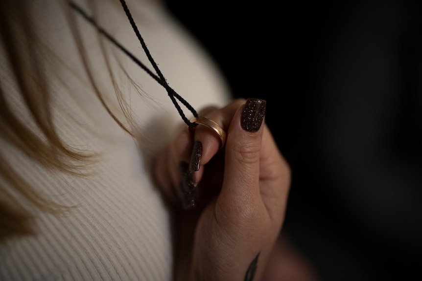 a close up of a woman's hand holding a wedding ring which is worn at the end of a necklace