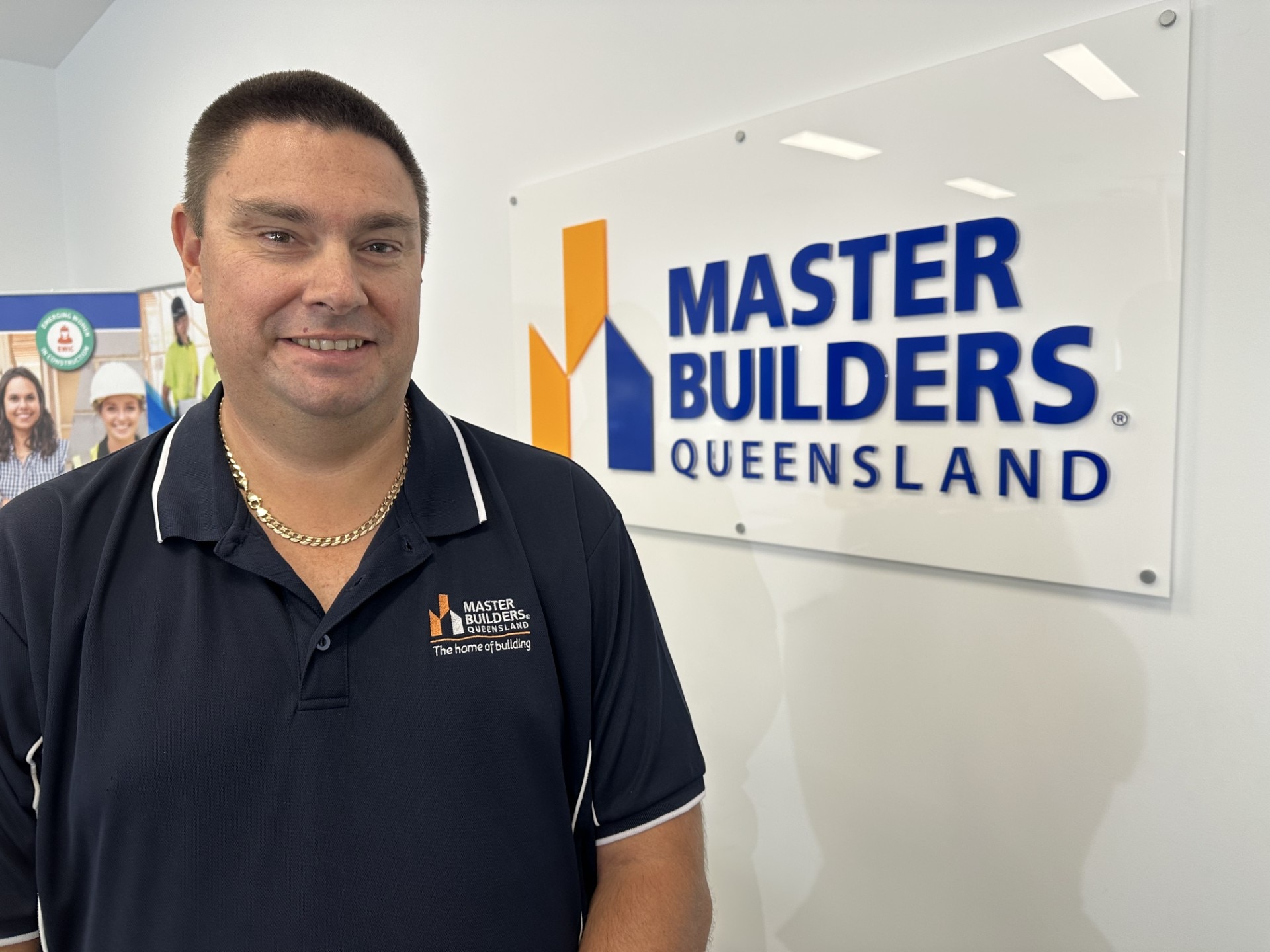 Un hombre de cabello oscuro con una camiseta polo con la marca se encuentra en una oficina con un cartel que dice 