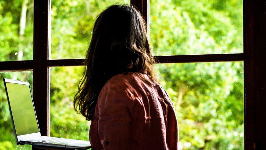 Woman sitting at home looking out a window onto nature.