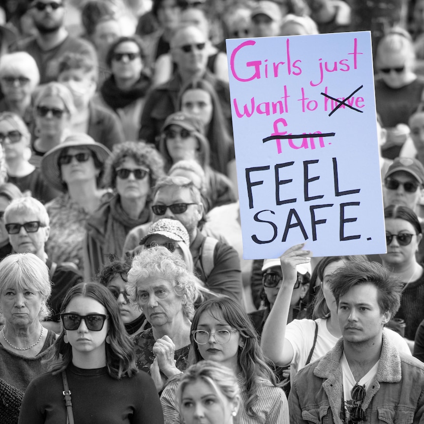 a crowd of protesters edited in black and white, a sign says girls just want to feel safe