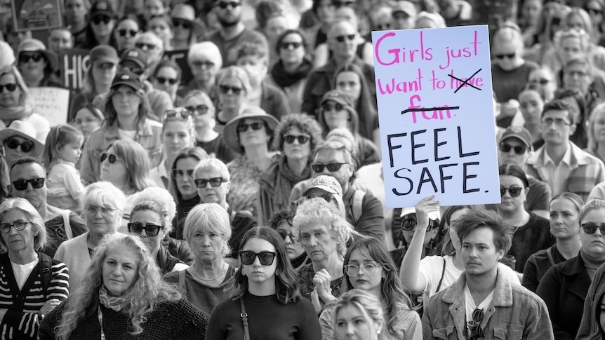 a crowd of protesters edited in black and white, a sign says girls just want to feel safe