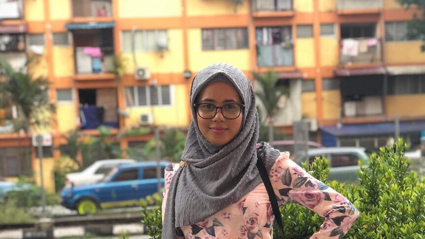 A woman in a hijab stands in front of apartment blocks in Malaysia.