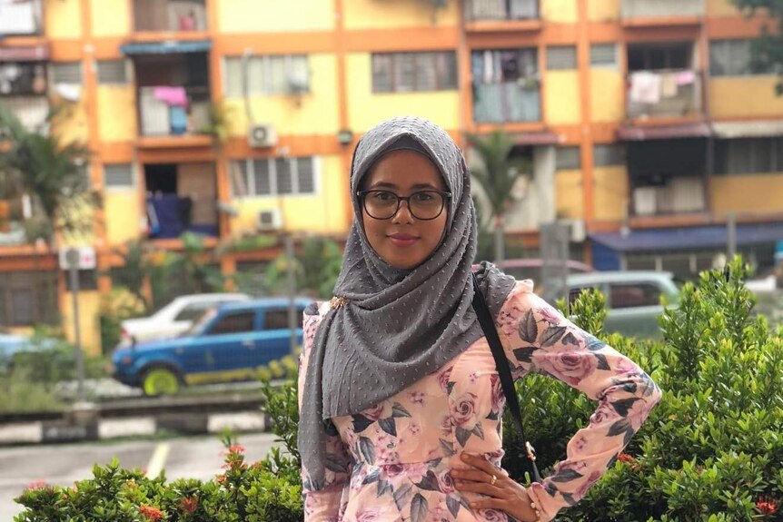 A woman in a hijab stands in front of apartment blocks in Malaysia.