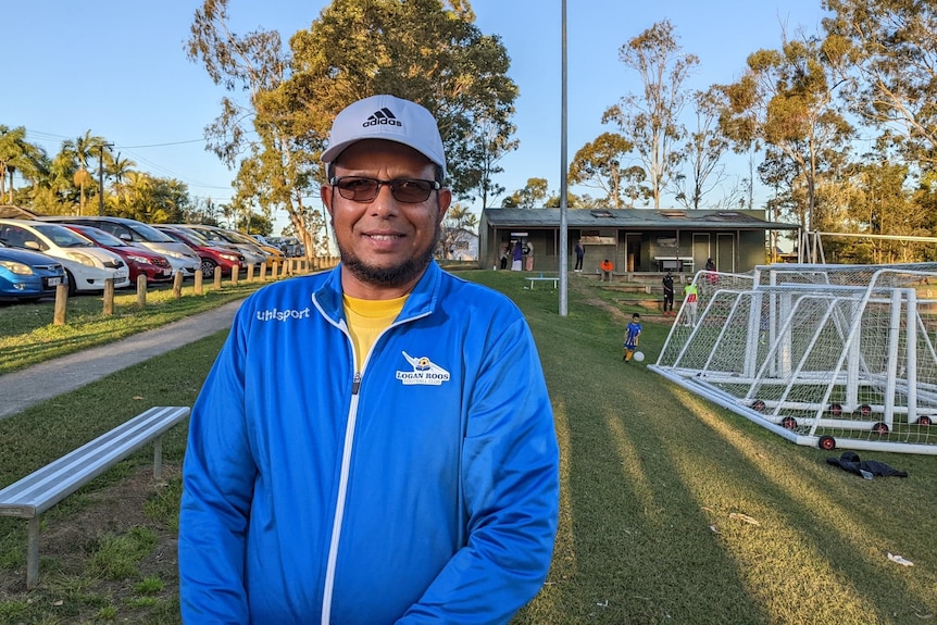 A man in a blue tracksuit stands at a football ground.