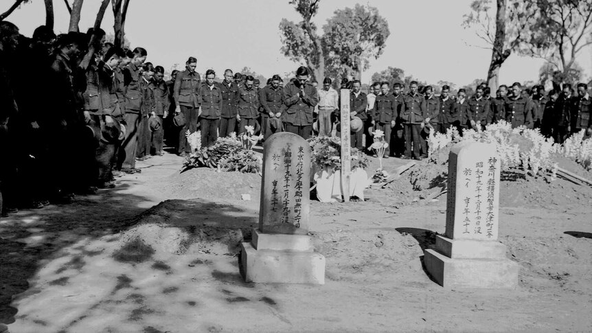 Black and white image of Japanese soldiers gathered solomnly around two headstones with Japanese writing.