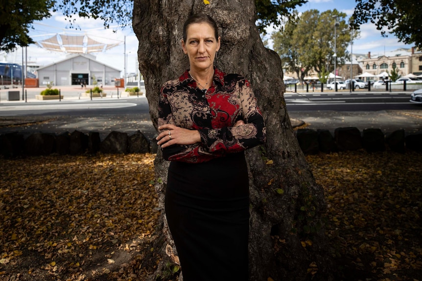 La femme se tient les bras croisés devant un arbre. 