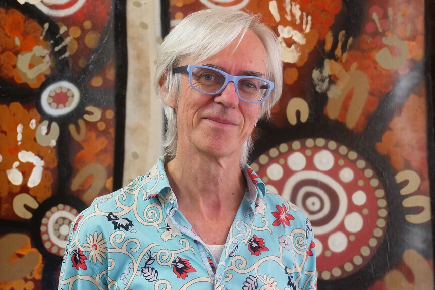 A man standings in front of a mural with Indigenous artwork. 