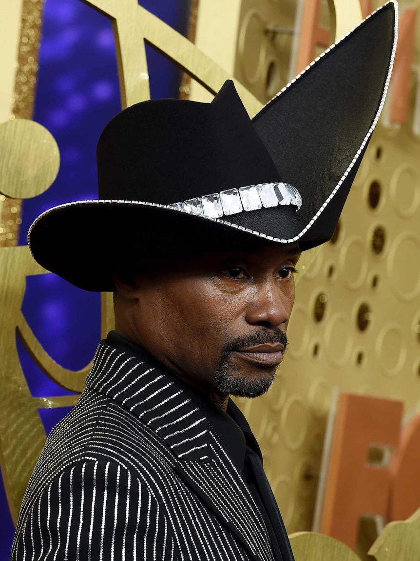 Billy Porter, wearing a large black hat which veers skyward on one side, looks fierce on the purple carpet.