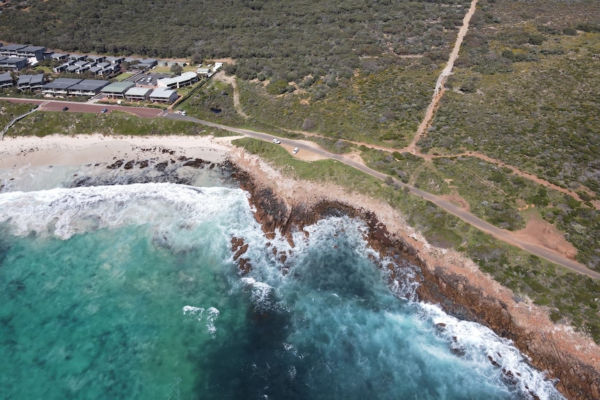 An aerial view of a coastline, some empty land and some housing developments to the left