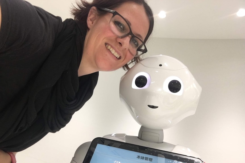 A woman smiles with a robot.