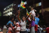 Zimbabweans stand on the back of a ute celebrate waving flags, smiling