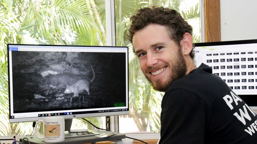An image of a man looking at a quoll pictured on a computer screen.
